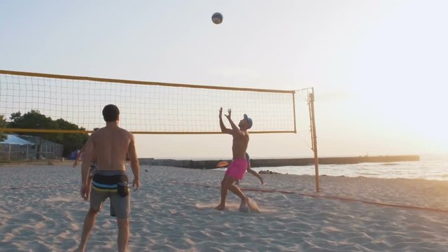 Group of people playing beach volleyball during sunrise or sunset