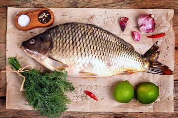 Fresh raw carp fish with lime, dill and garlic on old wooden background.
