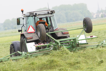Farmer uses tractor to spread hay on the field