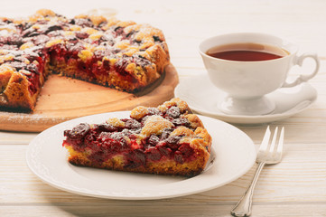 Cherry biscuit pie and cup of tea on white wooden background.
