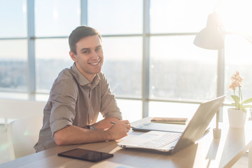 Man using laptop on his workplace. sitting, smiling, looking at camera.