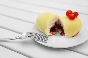 Cut dessert with red currant in white plate on light wooden table