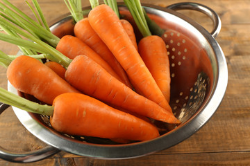 Fresh carrots in a colander on wooden table