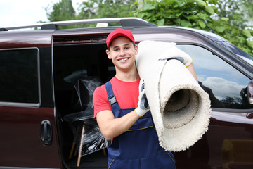 Male worker with carpet on car background
