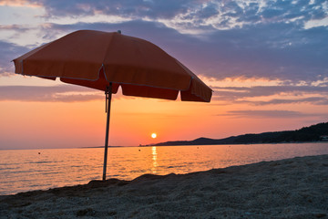 Sandy beach with one orange sunshade at sunset in Sithonia, Greece