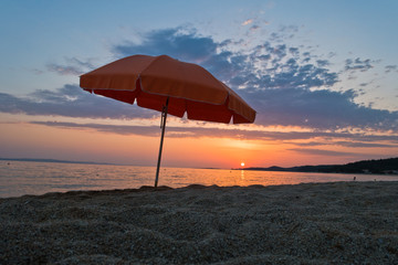 Sandy beach with one orange sunshade at sunset in Sithonia, Greece