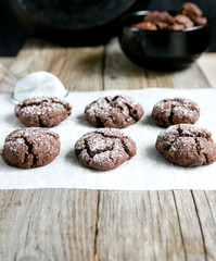 Chocolate cookies on kraft paper, sprinkled with powdered sugar on a wooden background