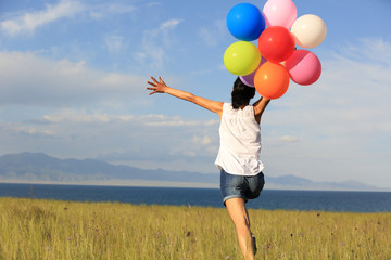 cheering young asian woman running on grassland with colored balloons