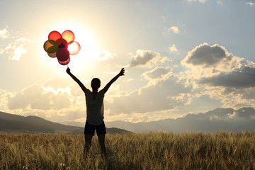 cheering young asian woman on sunset grassland with colored balloons