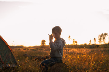 boy drinking juice at sunset, boy sitting near tent