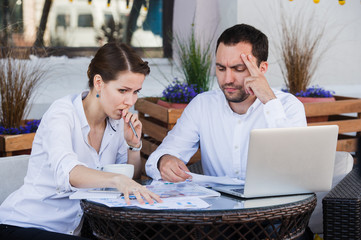 Male and female business colleagues working together on a hard problem at outdoors cafe. They have...
