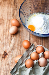 The image of eggs and flour on a wooden table.