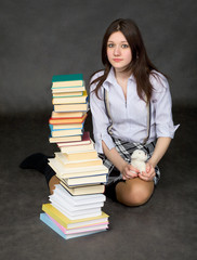 The beautiful schoolgirl sits near a pile of books