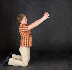 Amusing young man is kneeling and stretch hands to something