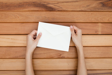woman hand hold a envelope and post card on the wood desk, top v