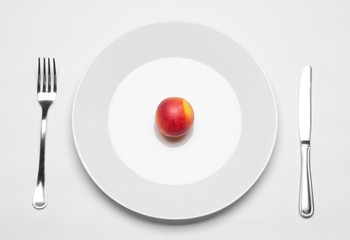 Healthy eating in the restaurant and diet Topic: beautiful ripe nectarine on a white plate with a metal knife and fork lies on an isolated white table in studio top view