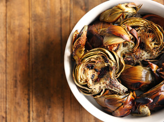 Baked artichokes with spices in a bowl on wooden background