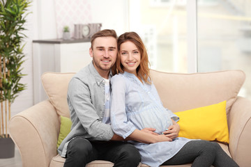 Obraz premium Happy pregnant woman and her husband on a sofa at home