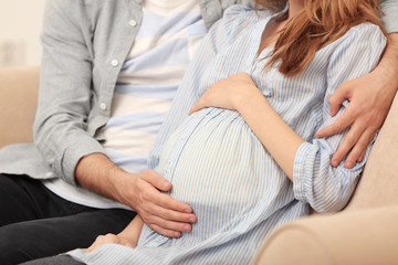 Pregnant woman and her husband on sofa at home, closeup