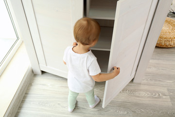 Cute baby girl playing with a wooden cupboard