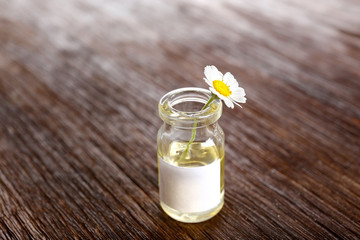 Healing chamomile flower in small glass bottle on brown wooden background