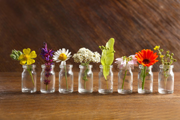 Different healing flowers in small glass bottles on wooden background