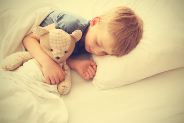 Adorable little boy sleeping with teddy bear in bed