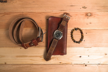 Men's accessories with brown leather wallet, bracelet, belt and watch on wood background
