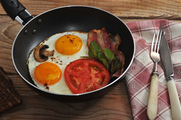bacon and eggs and mushrooms with the pan on wooden background i
