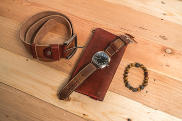 Men's accessories with brown leather wallet, bracelet, belt and watch on wood background
