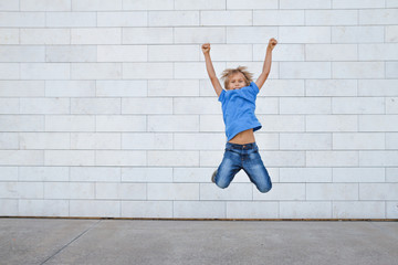 Happy little boy jumping. Urban gray background. People, childhood, happiness, freedom, movement...