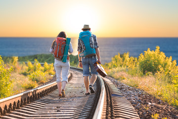 Young Couple Man and Woman with Backpacks and Guitar in casual Travel Clothes walking along...