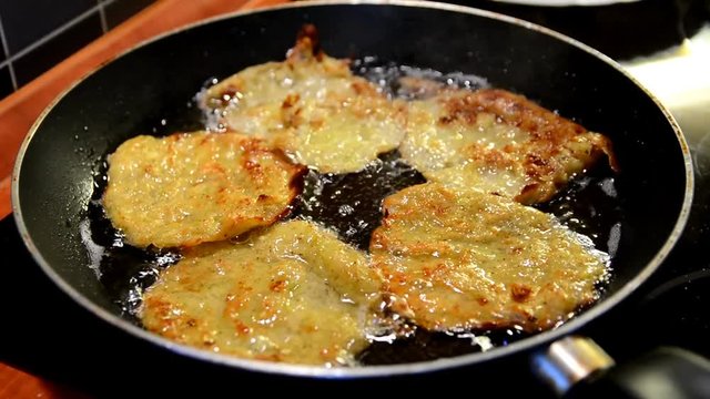 Frying zucchini potatoes pancakes in oil in a frying pan.