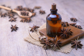 Essential aroma anise oil in a glass bottle with dried star anise on wooden spoon and background.