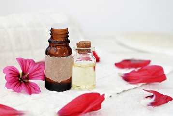 Essential oil bottles. Flower extract, pink petals, handcrafted empty label, white bathroom towel background.