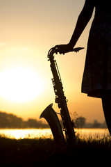 silhouette of a woman in a dress on a background of a beautiful sun set and the sky saxophone on...
