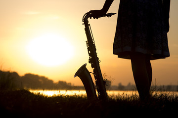 silhouette of a woman in a dress on a background of a beautiful sun set and the sky saxophone on...