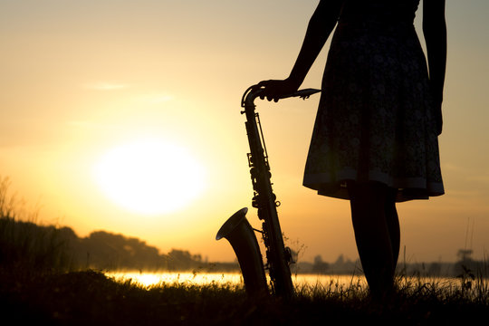 silhouette of a woman in a dress on a background of a beautiful sun set and the sky saxophone on the grass and enjoy the view