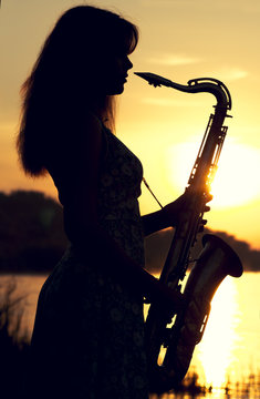 silhouette of a girl in a dress with a brass musical instrument in his hands looking thoughtfully into the distance