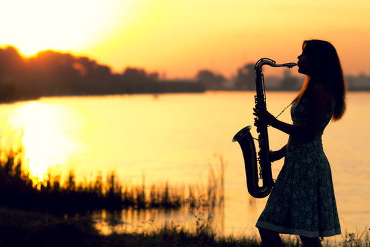 silhouette of a girl on the background of the dawn of the landscape on the banks of the river who found joy in his hobby - music