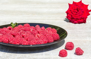 Raspberries on a black plate and red rose