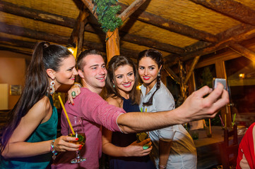 Young beautiful people with cocktails in bar taking selfie