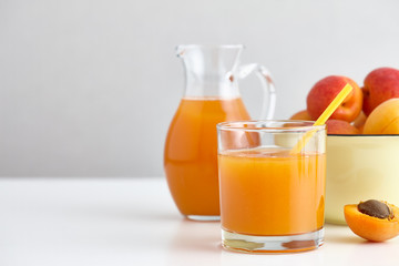 Glass and jug of fresh apricot juice on white table