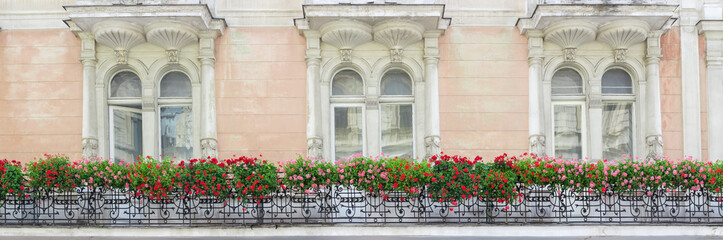 Fototapeta na wymiar Forged balcony with flowers on the wall of old house