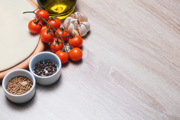 Dough basis for the pizza on a wooden board and cherry tomatoes, olive oil, onions, garlic.
