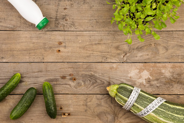 marrow squash, measure tape, bottle of water and cucumbers on brown wooden table