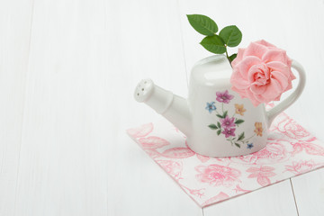 Rose Flower In Porcelain Watering Can. White Table.