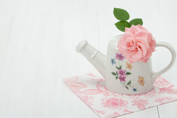 Rose Flower In Porcelain Watering Can. White Table.
