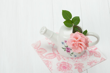 Rose Flower In Porcelain Watering Can. White Table.