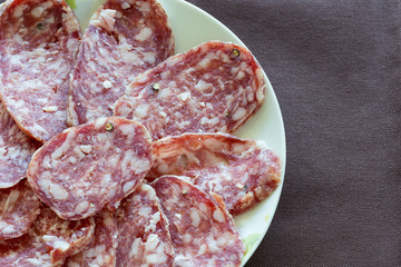 Fette di salame di maiale nostrano su piatto bianco e tovaglia marrone